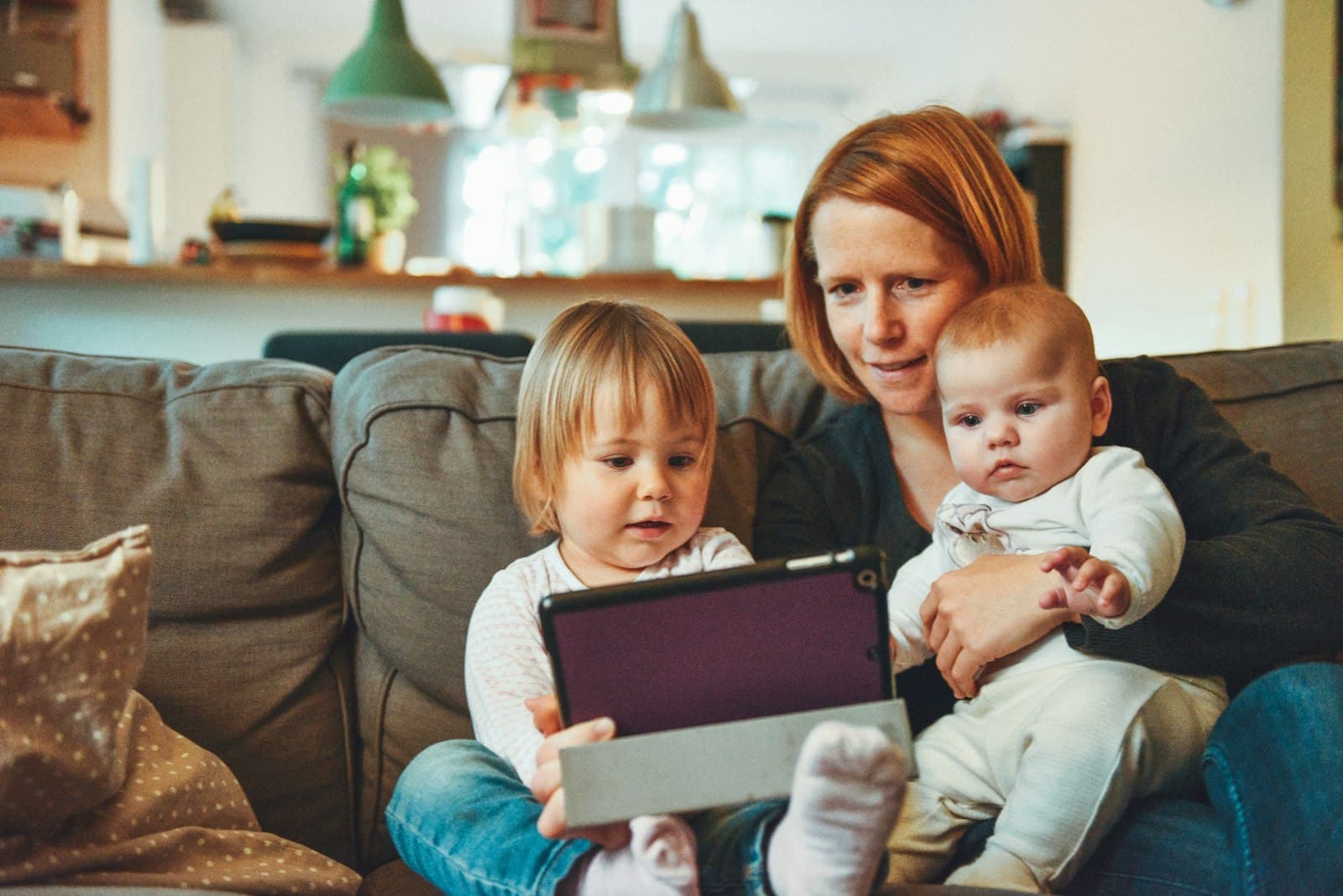 A parent on the couch with a toddler and a baby, sharing a quiet moment together at home