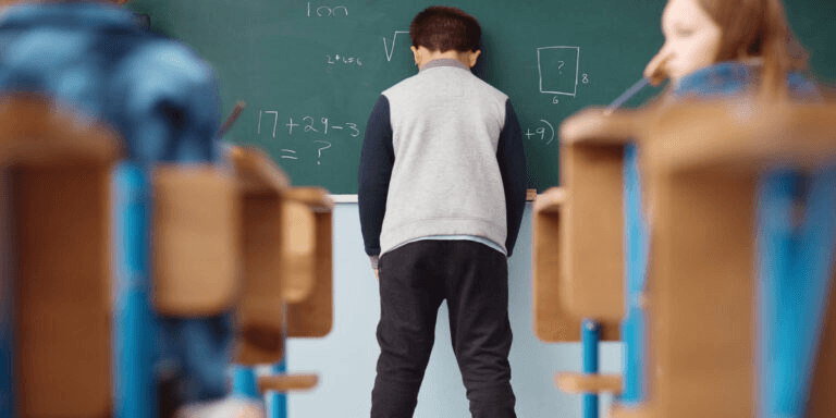 A young boy leaning his head against a classroom chalkboard, reflecting the frustration a child may feel when communication challenges go unsupported