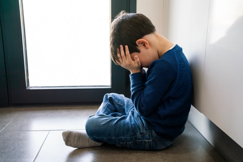 A young child sitting on the floor with his head in his hands, capturing the frustration children can feel when communication is hard